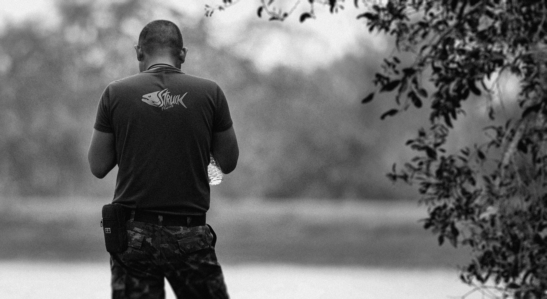 Pescador de costas em foto preto e branco em ambiente natural, transmitindo o espírito outdoor da marca Struck Fishing